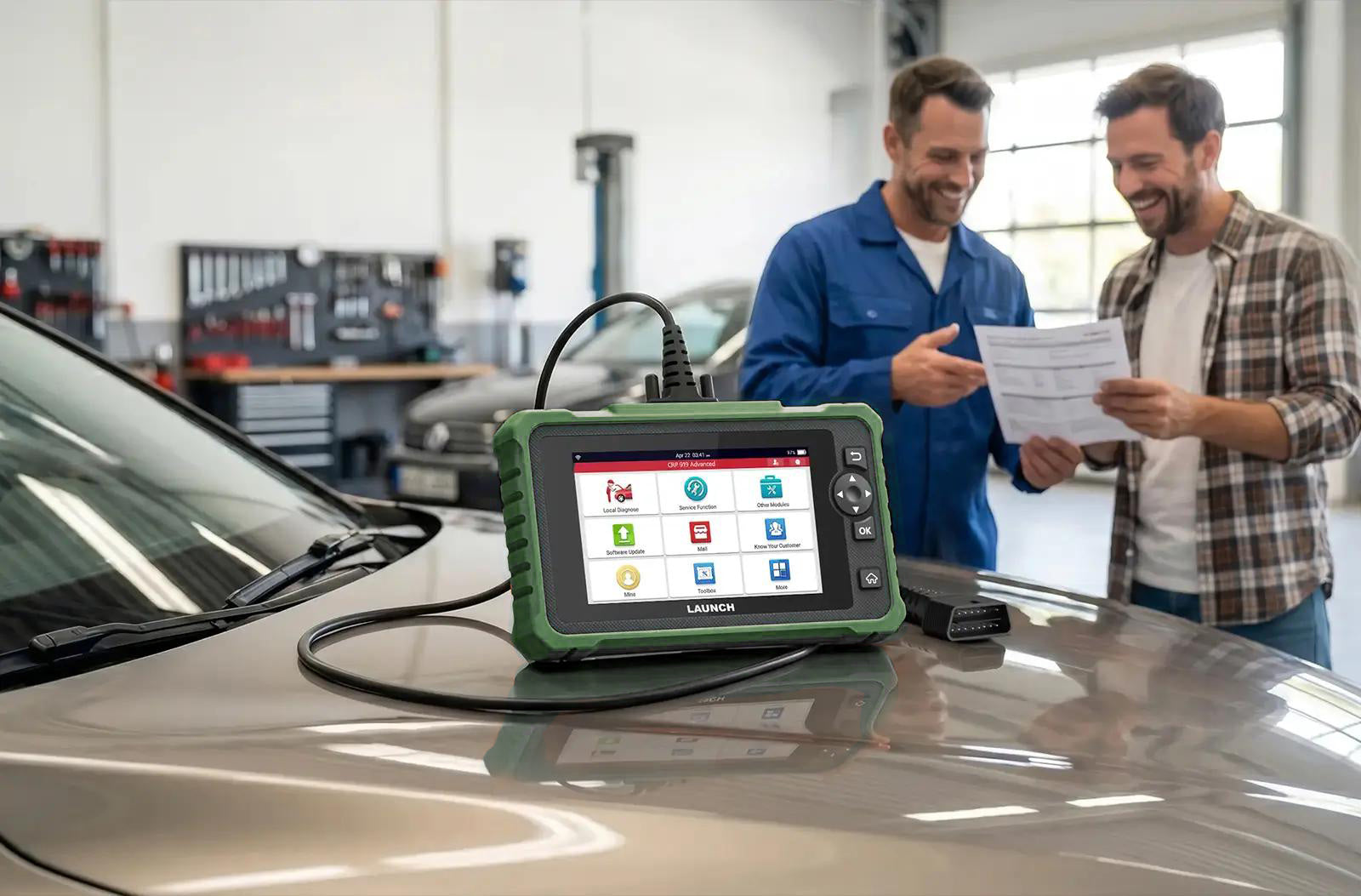 A LAUNCH CRP 919 Advanced diagnostic tool resting on the hood of a car inside a repair shop. In the background, a mechanic in blue overalls and a customer are smiling while looking over a printed diagnostic report together.