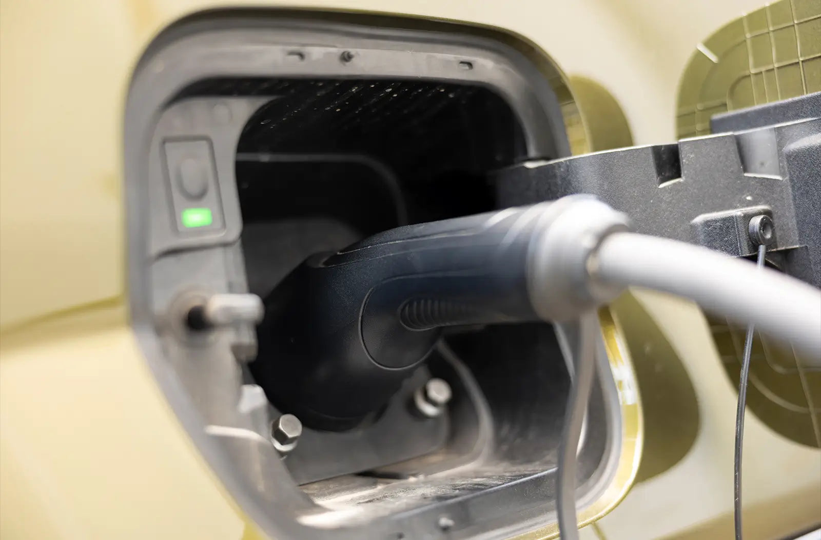 A close-up shot of a black charging cable connector plugged firmly into the side charging port of a modern electric vehicle.