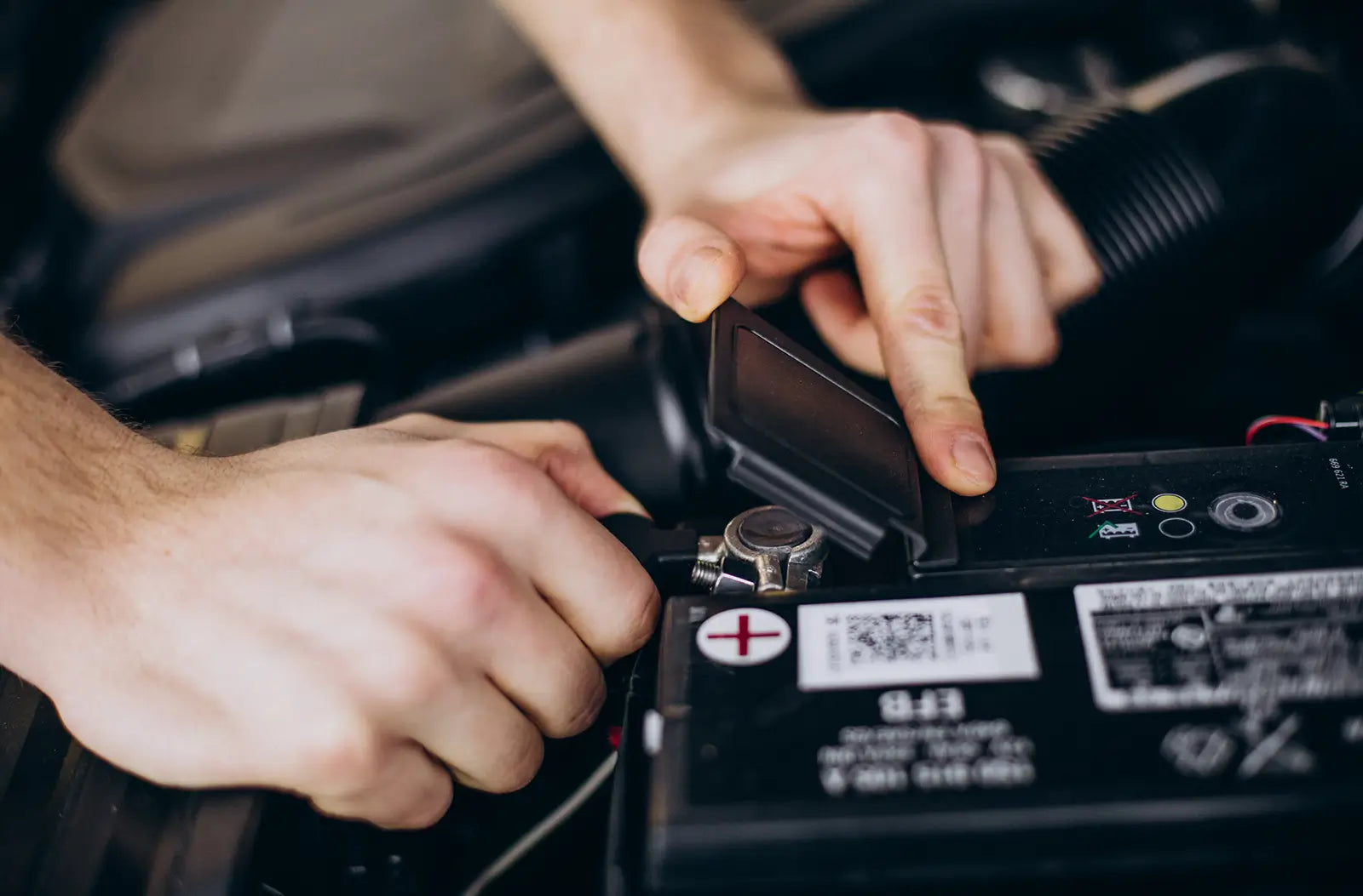 Shows a clean, new white car battery with red and black terminal covers installed inside an open vehicle engine bay.