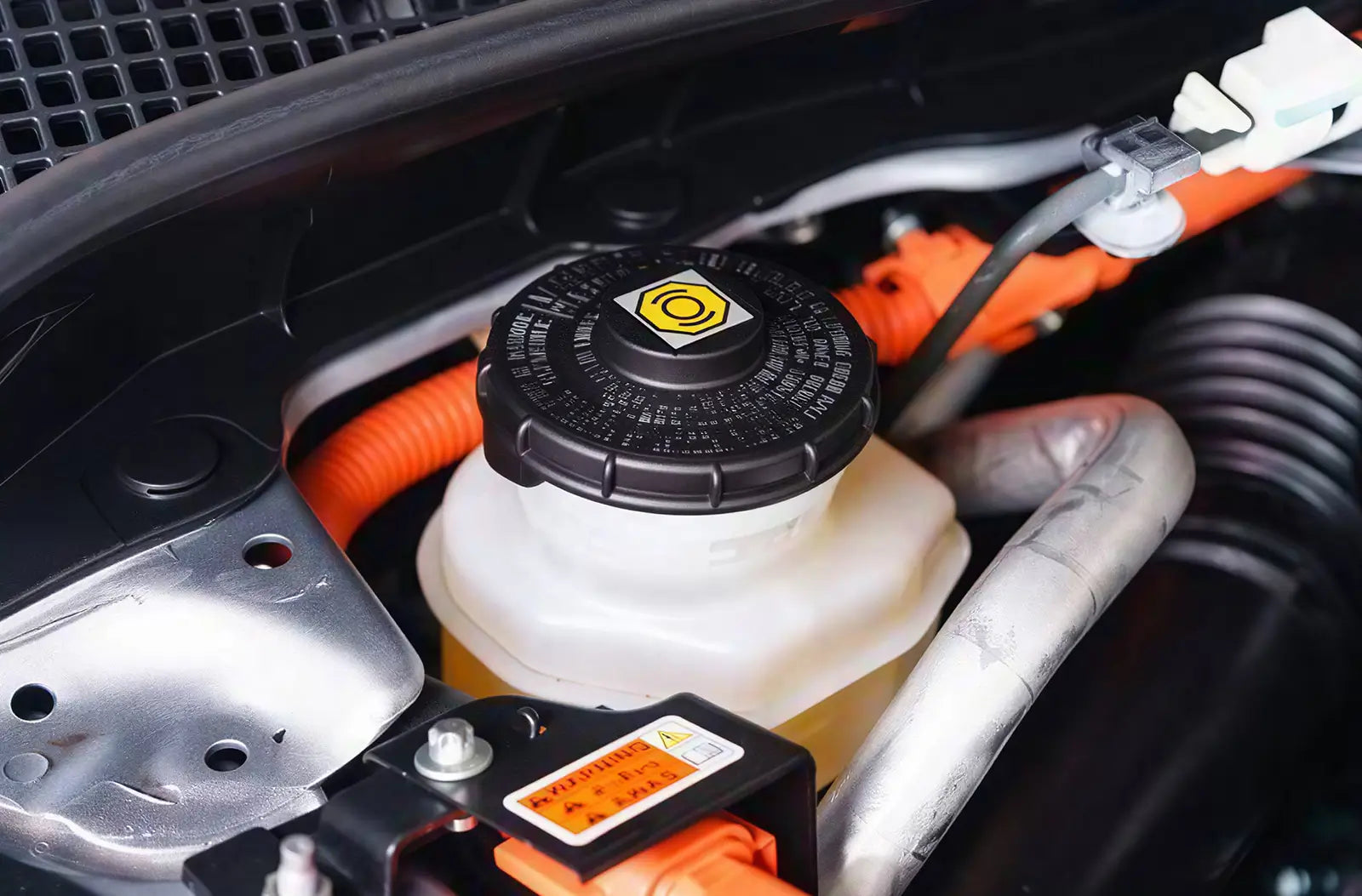 Shows a mechanic working in a garage, using a long wrench to open a brake caliper bleeder valve behind a car's metallic brake disc assembly.
