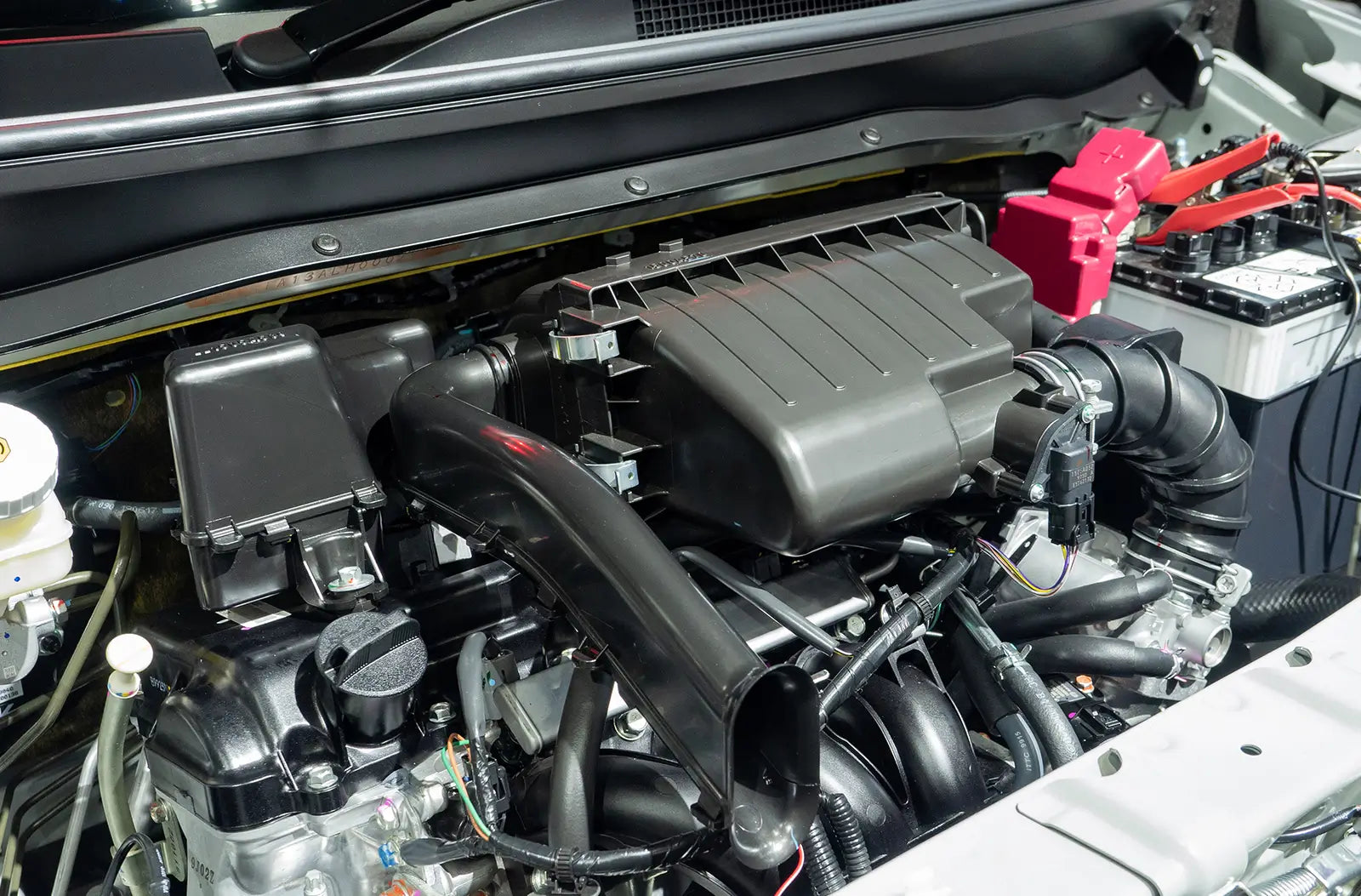 A view under the open hood of a car, showing the metallic alternator belt pulley system nestled deep within the complex engine compartment.