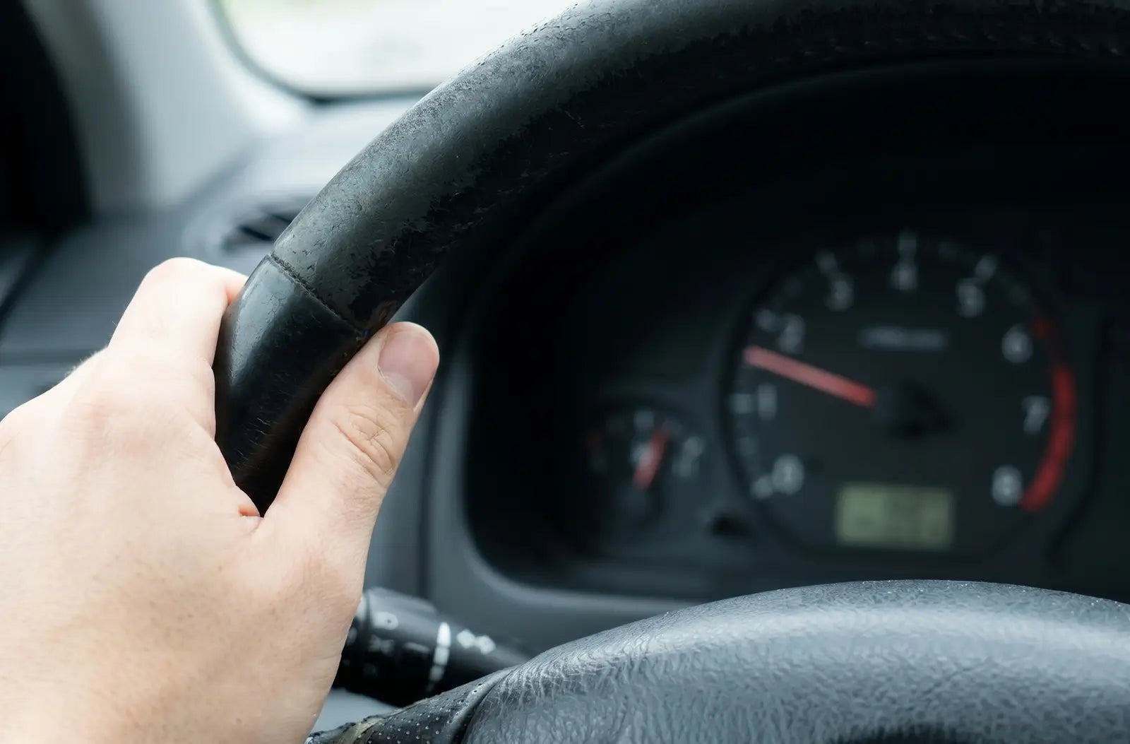 Close-up shot of a car's analog instrument panel showing a fluctuating engine tachometer gauge needle hovering near low RPM numbers.