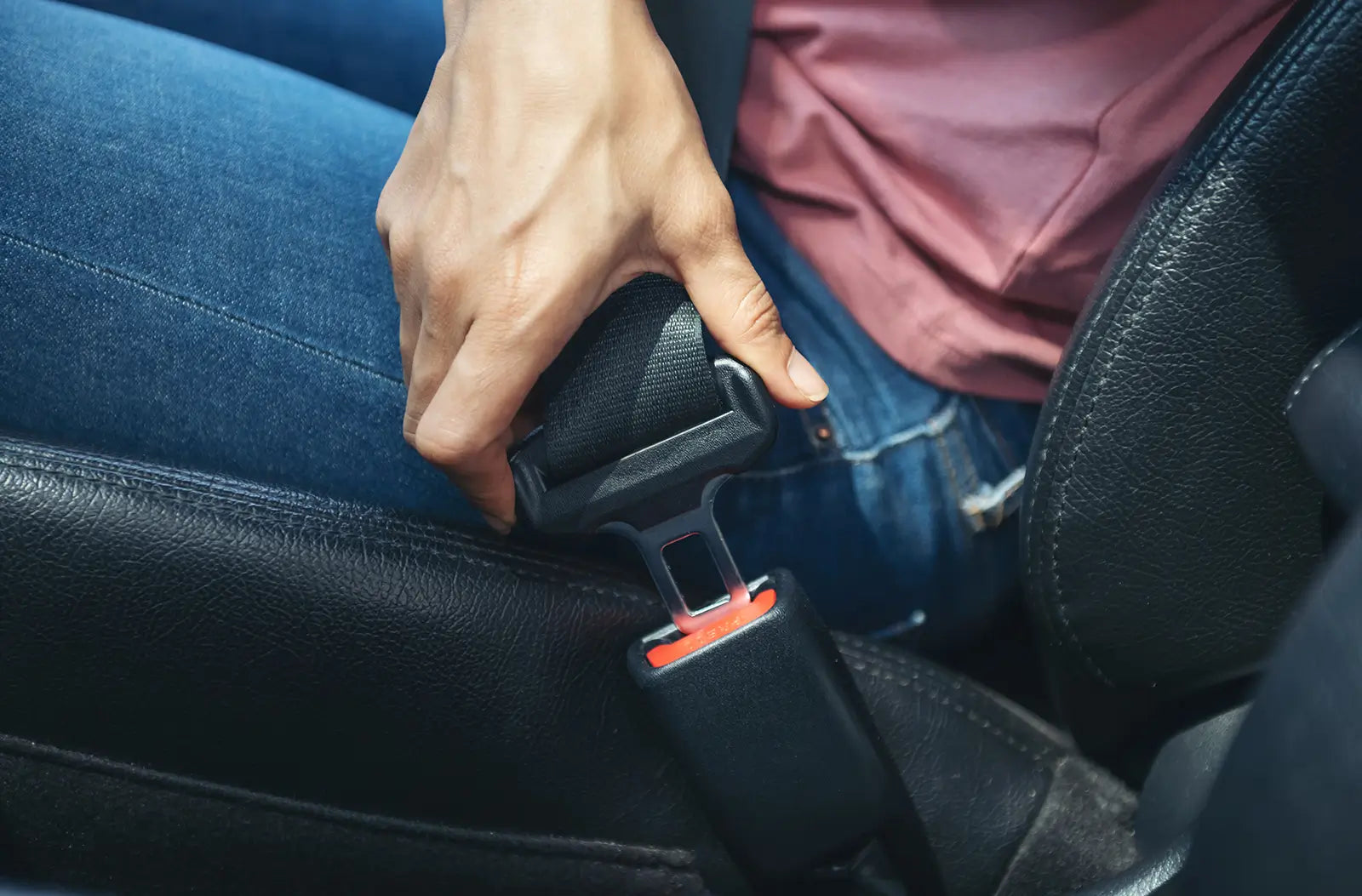 Close-up view of a car's interior B-pillar, showing a black seat belt strap threading directly into the mechanical plastic guide assembly.