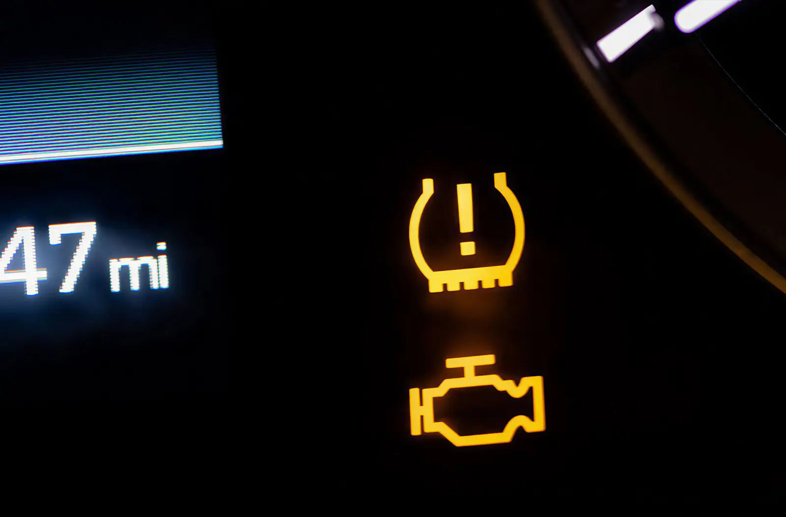 A view from behind the steering wheel showcasing a distinct yellow "Low Tire Pressure / TPMS" exclamation symbol illuminated on the center dashboard display.