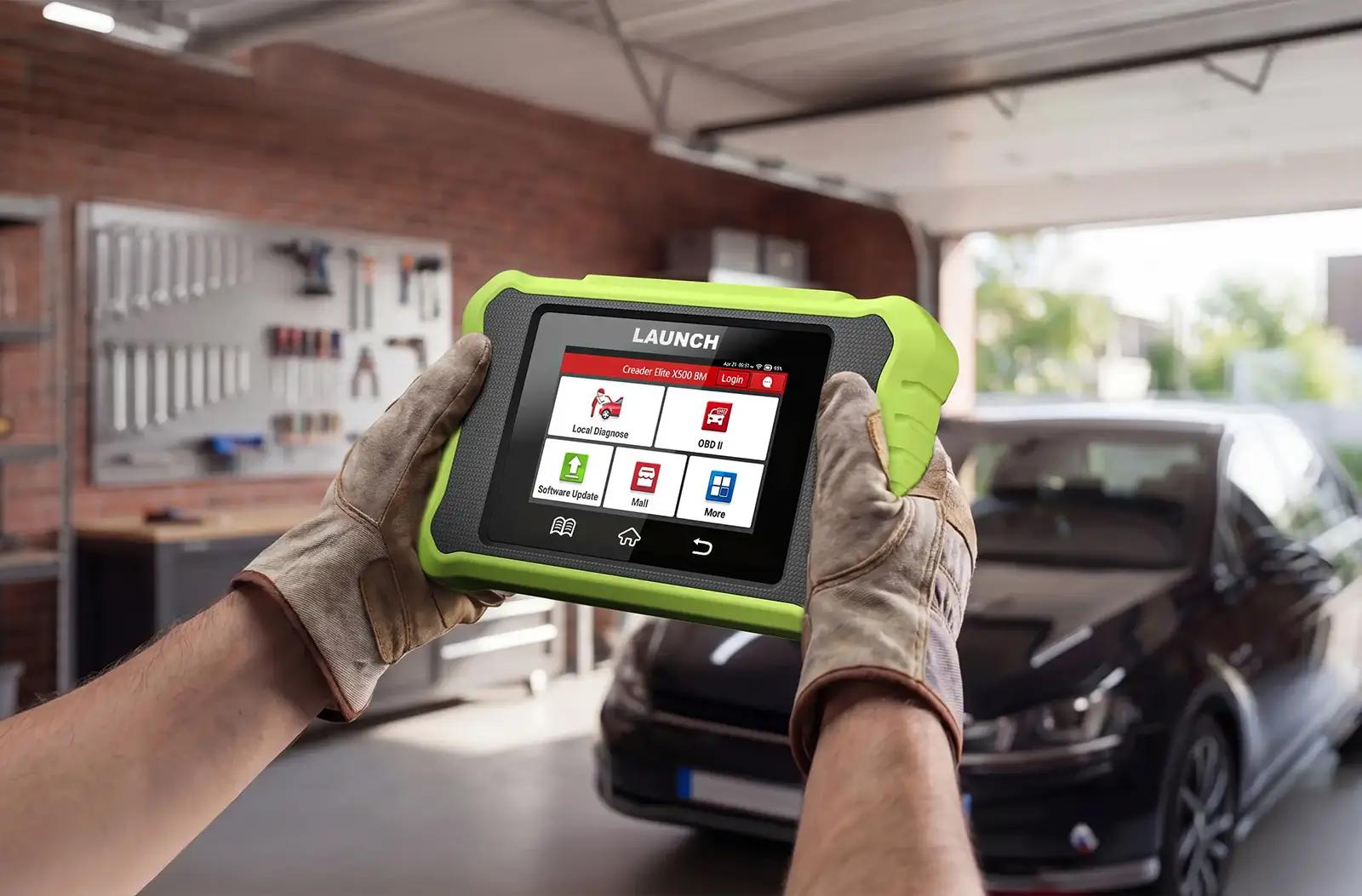 A person wearing work gloves holding a LAUNCH Creader Elite X500 BM diagnostic tool. The device is enclosed in a bright green protective casing, and its touchscreen displays menu icons such as Local Diagnose and OBD II.