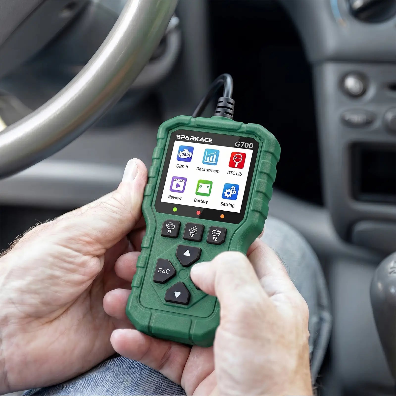 This image shows a person's hands holding and operating a Sparkace G700 diagnostic scanner inside a car. The handheld device is powered on, displaying its main menu while being used for vehicle troubleshooting.