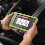 A person holding a LAUNCH Creader Elite X500 BM diagnostic tool over a car engine bay. The device features a lime green rugged bumper and a touchscreen displaying menu options like Local Diagnose, OBD II, and Software Update.
