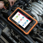 A LAUNCH CRP 919 Advanced diagnostic tablet resting on a car engine while being used for vehicle maintenance. The device features a rugged orange casing, a touchscreen with menu icons like Service Function and Local Diagnose, and is connected to the vehicle via a black OBD II cable.